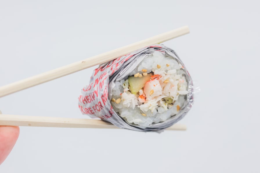 Person Holding Chopsticks with Sushi Wrapped in Paper